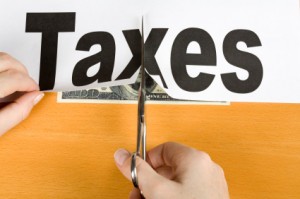 Picture of scissors cutting a piece of paper with taxes written on it.