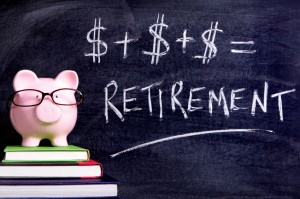Picture of Pink piggy bank with glasses standing on books next to a blackboard with simple retirement formula. Sharp focus on the piggy bank.