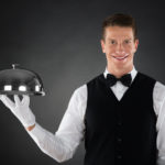 Portrait Of Happy Butler Holding Stainless Steel Cloche Over Tray