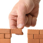 Picture of hand adding brick to a gap in the wall isolated on a white background