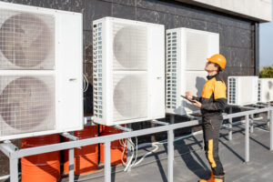 Professional workman in protective clothing adjusting the outdoor unit of the air conditioner or heat pump with digital tablet